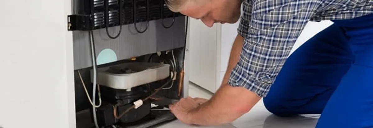 Refrigerator repair technician servicing the compressor and condenser area in Milwaukee, WI